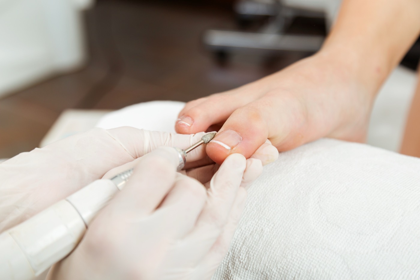 A gloved technician using an electric file on a toenail