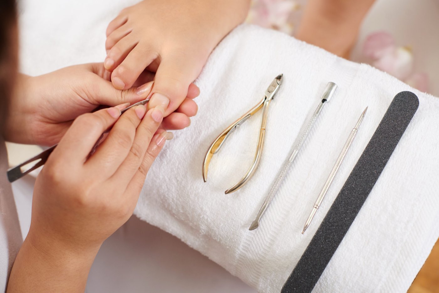 Cuticle nippers, a pusher and a file laid out on a towel beside a client's foot